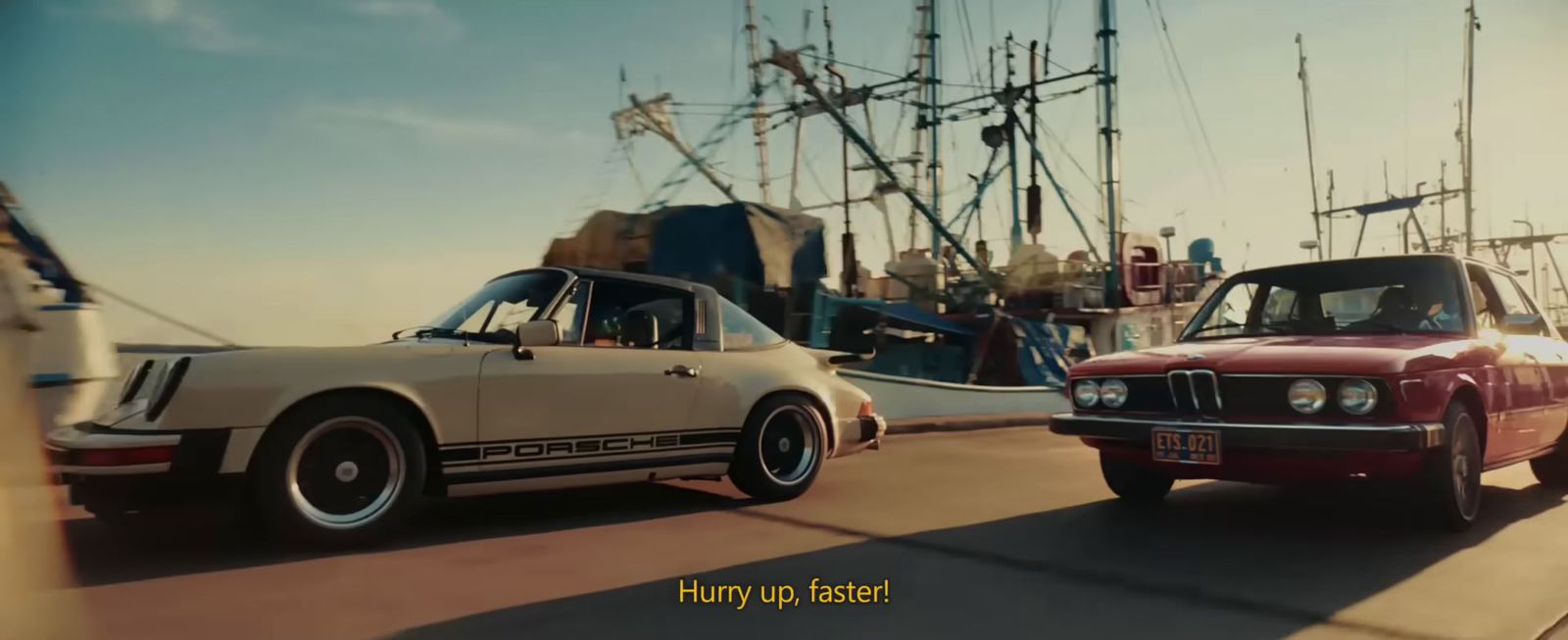 two cars driving down a street next to a boat