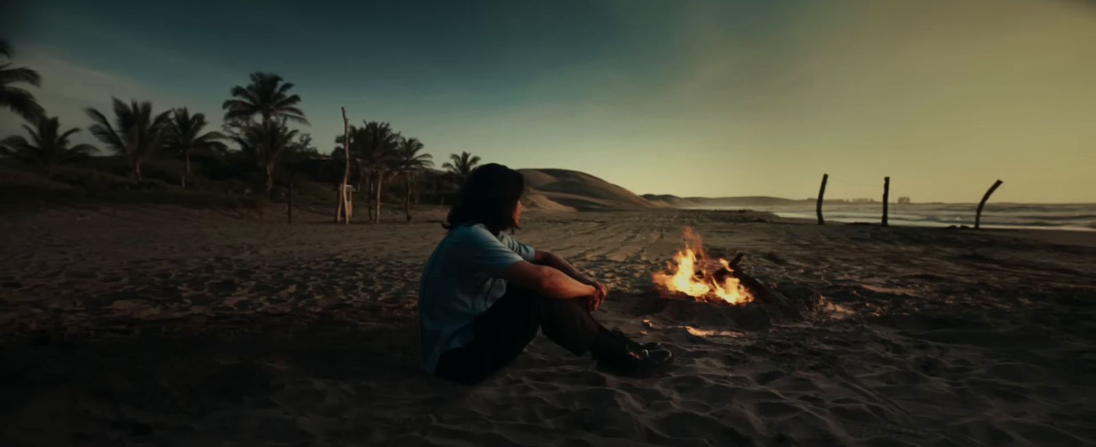 a man sitting in front of a fire on a beach