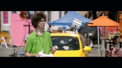 a woman in a green shirt standing next to a yellow car