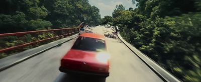 a red car driving down a road next to a forest