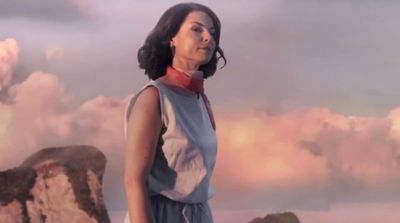 a woman standing on top of a mountain under a cloudy sky