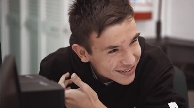 a young man smiles as he looks at a computer screen