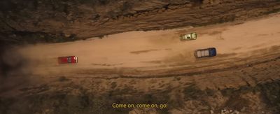 three cars driving down a dirt road next to a cliff