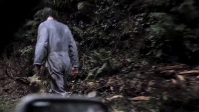 a man walking down a dirt road next to a forest