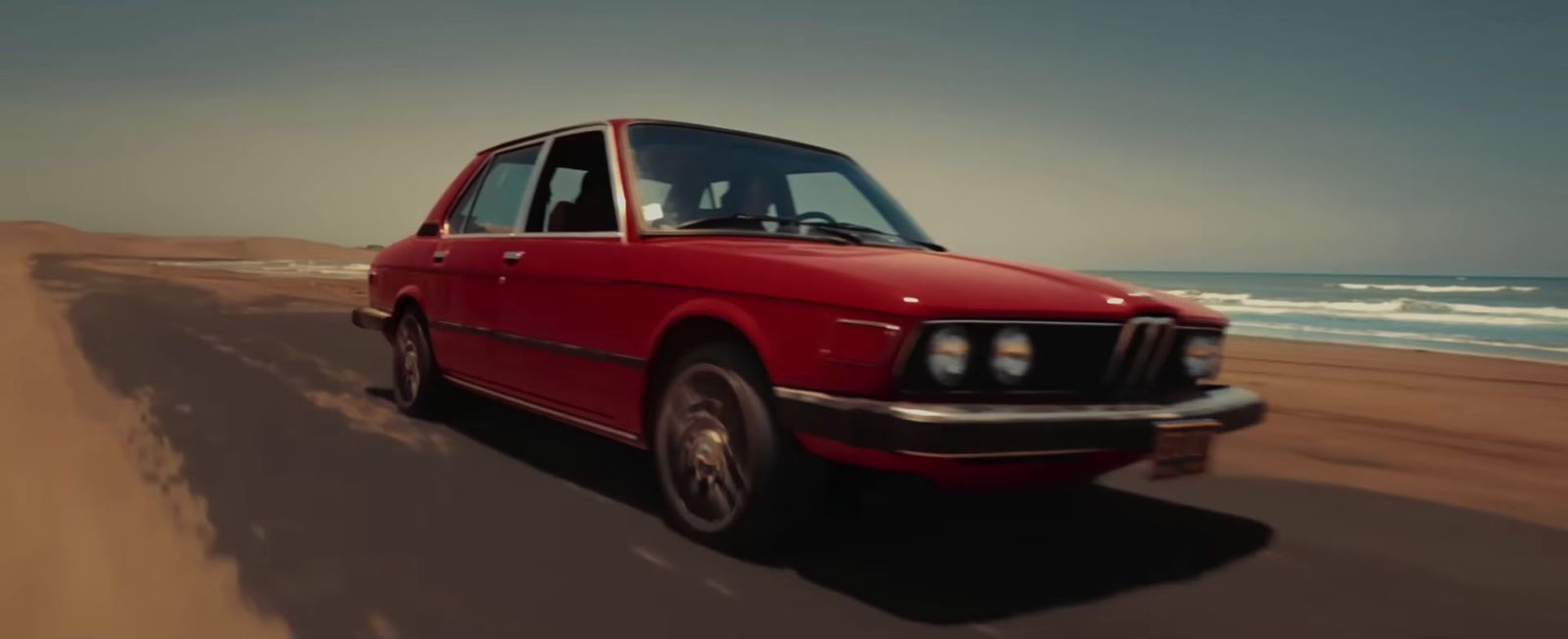 a red car driving down a sandy beach