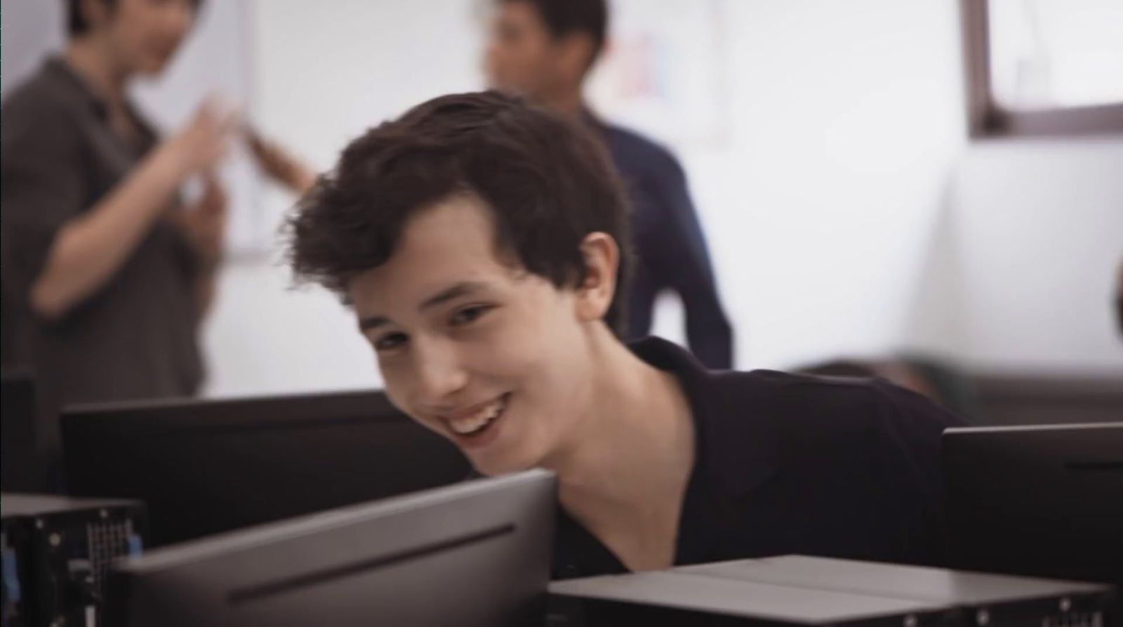 a smiling young man sitting in front of a computer monitor