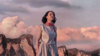 a woman standing on top of a mountain under a cloudy sky