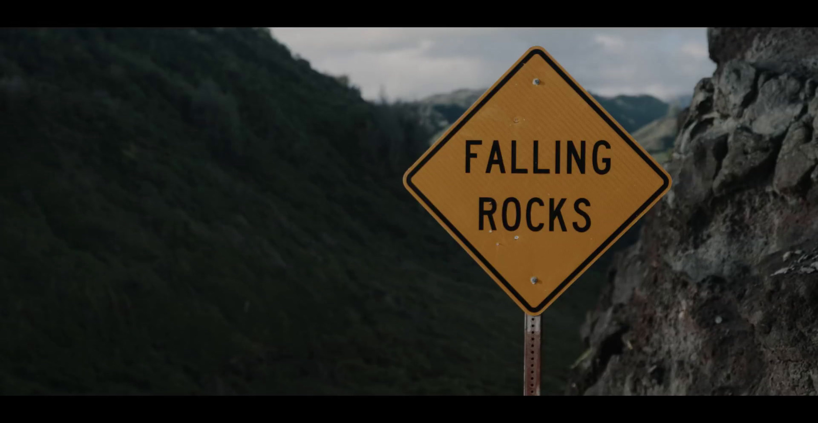 a yellow falling rocks sign sitting on the side of a mountain