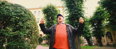 a man in an orange shirt and black jacket standing in front of trees