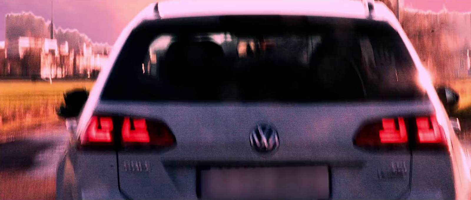 the back end of a silver car driving down a street