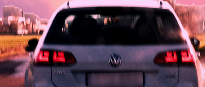 the back end of a silver car driving down a street