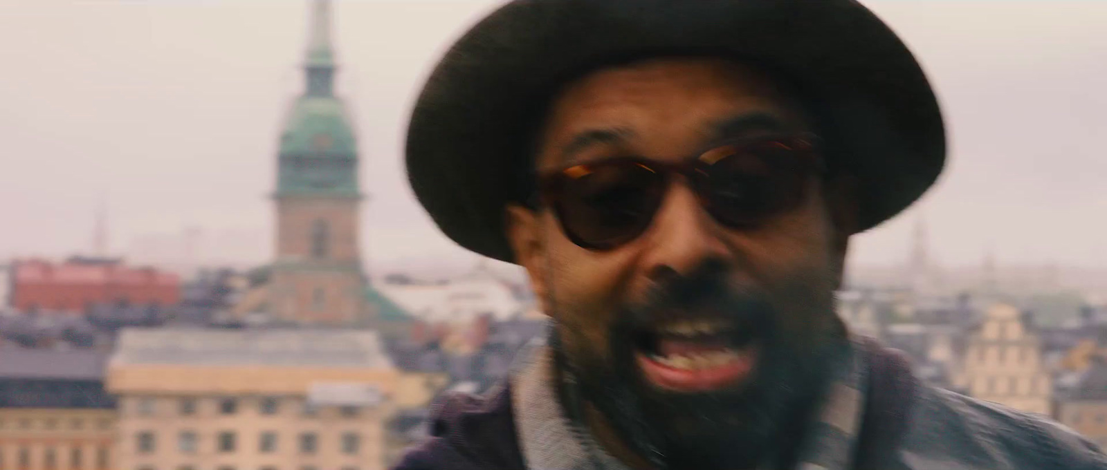 a man wearing a hat and sunglasses with a city in the background