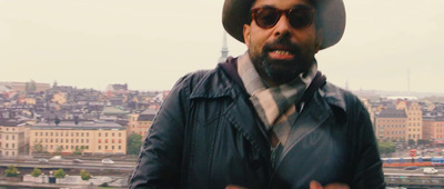 a man wearing a hat and sunglasses standing in front of a city