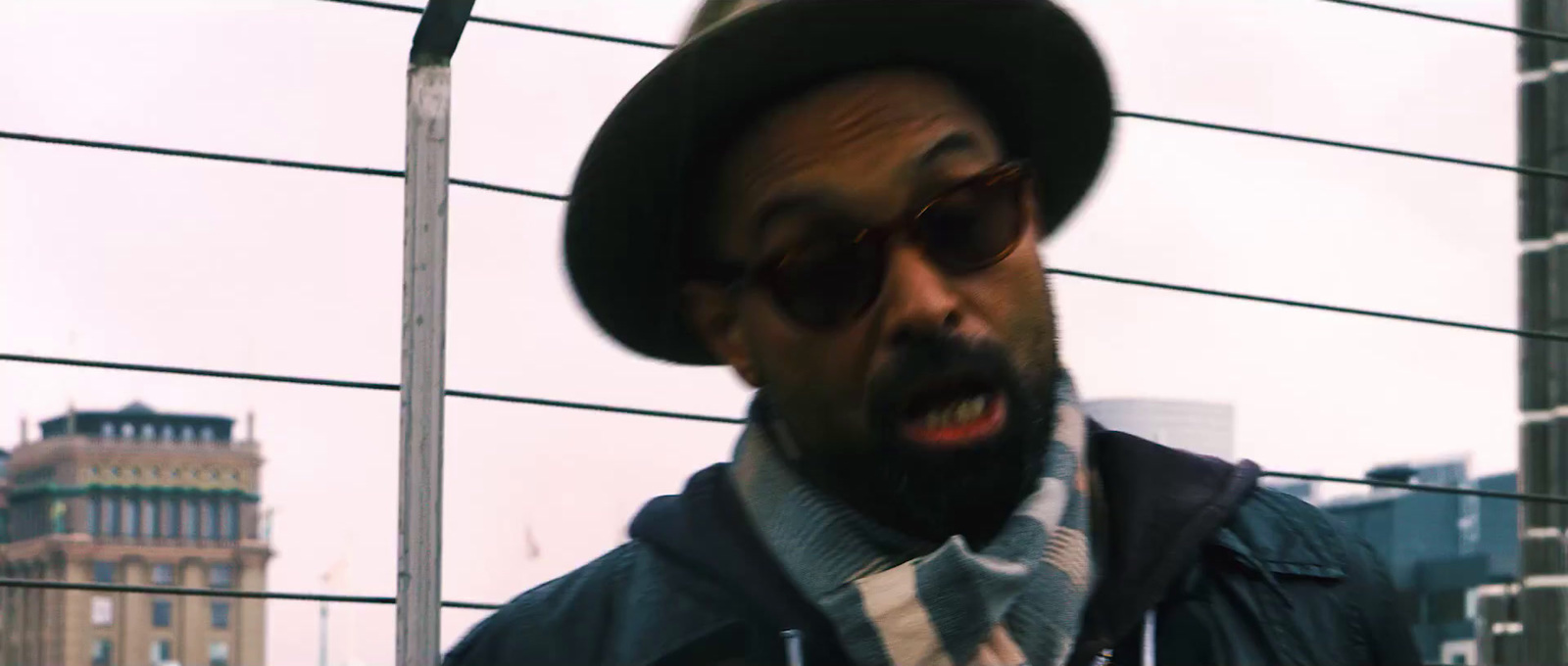 a man wearing a hat and glasses standing in front of a building