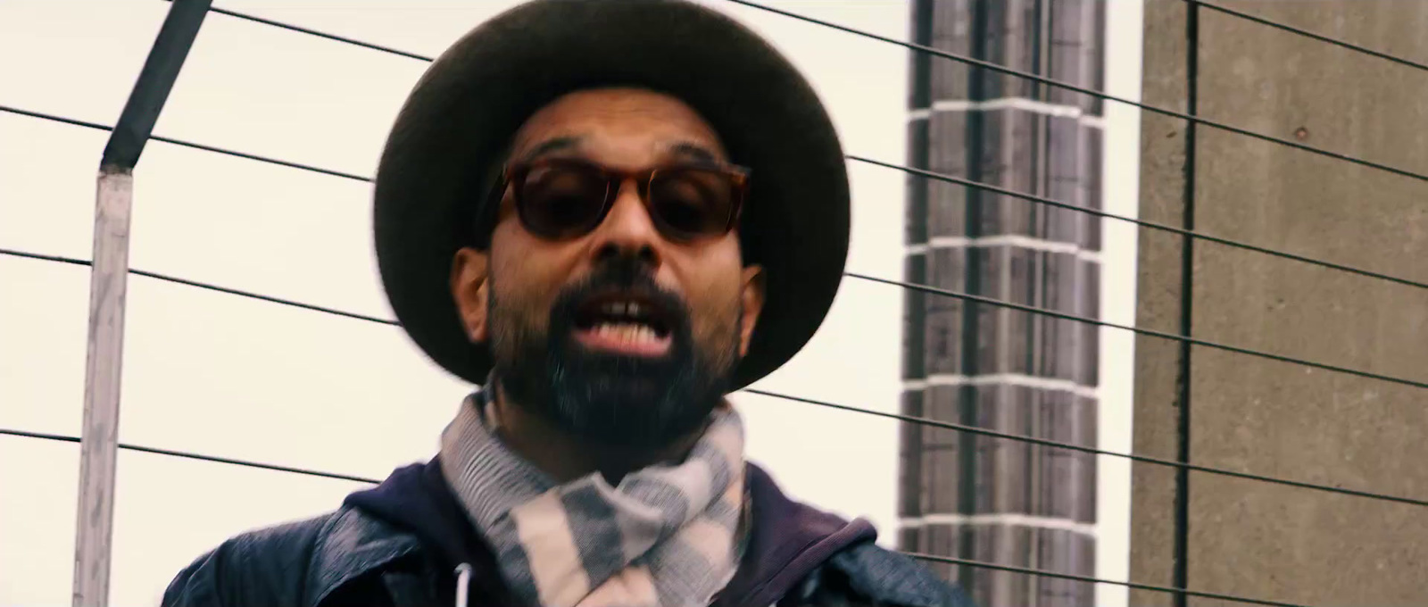 a man wearing a hat and sunglasses standing in front of a building