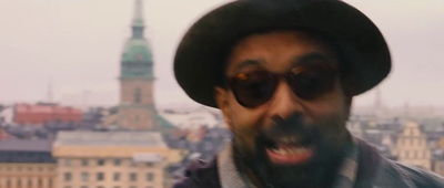 a man wearing a hat and sunglasses with a city in the background