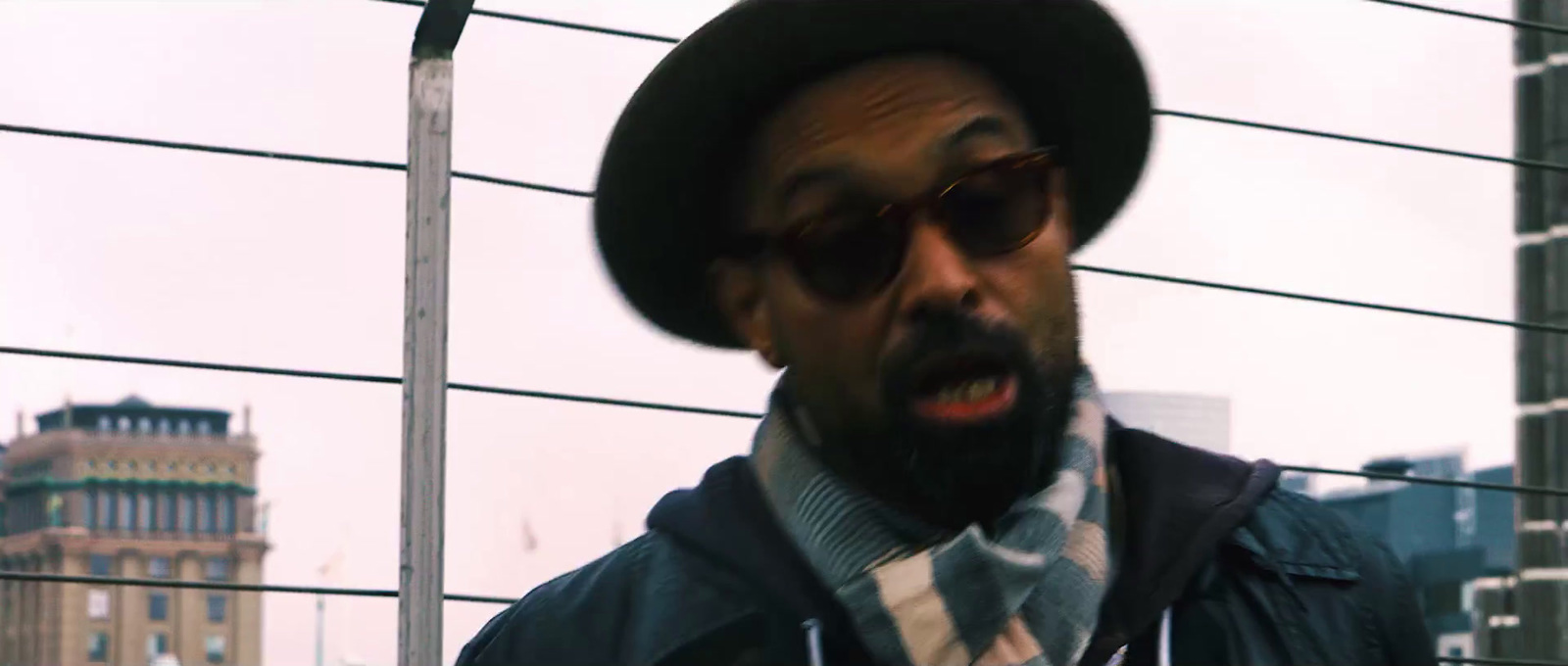 a man wearing a hat and sunglasses standing in front of a building