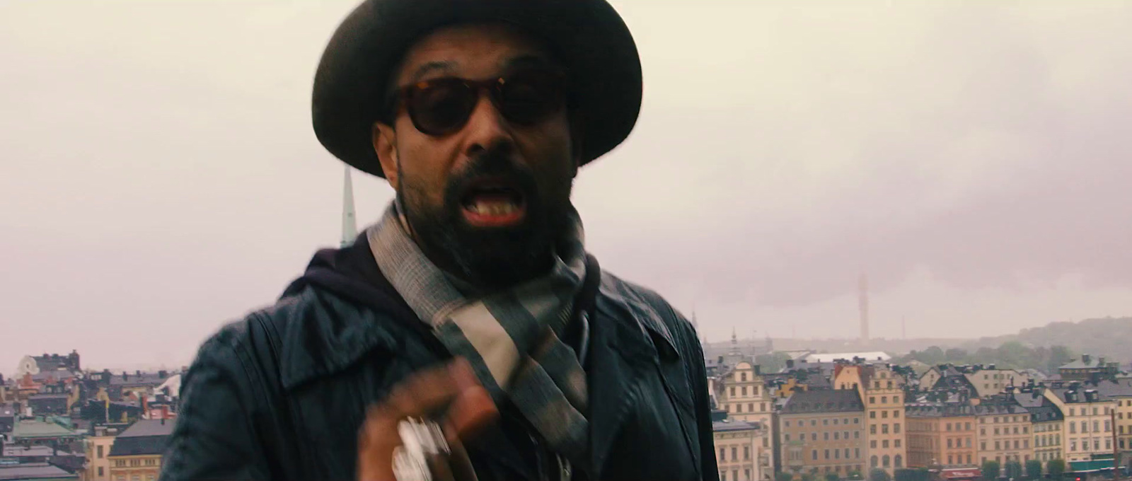 a man wearing a hat and a tie in front of a city