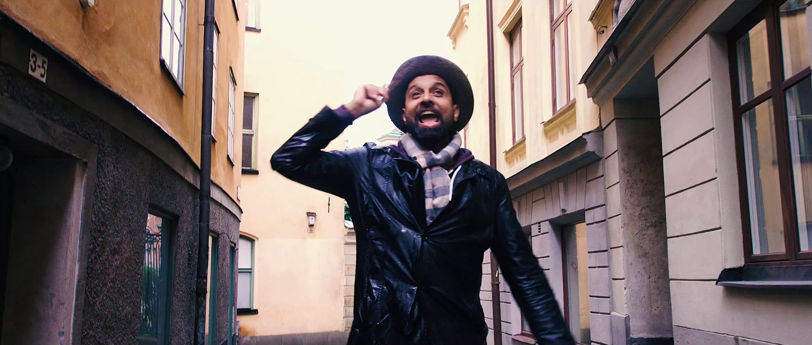 a man in a black jacket and hat walking down a street