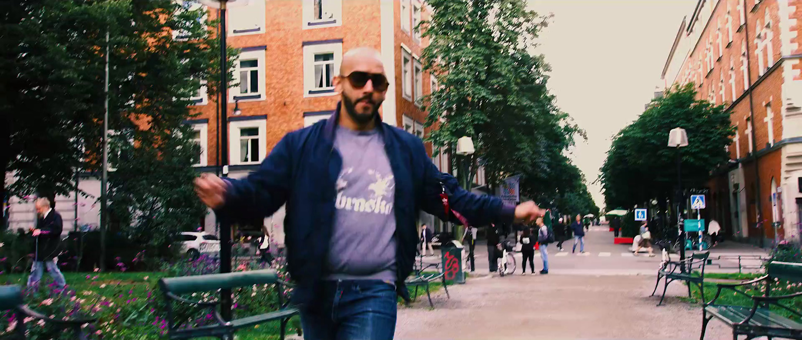 a man in a blue jacket and sunglasses walking down a street