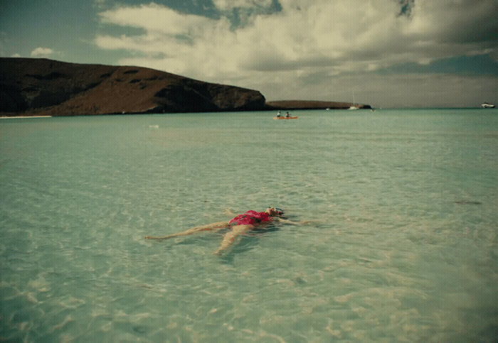 a woman floating in the ocean wearing a pink shirt