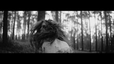 a woman with long hair walking through a forest