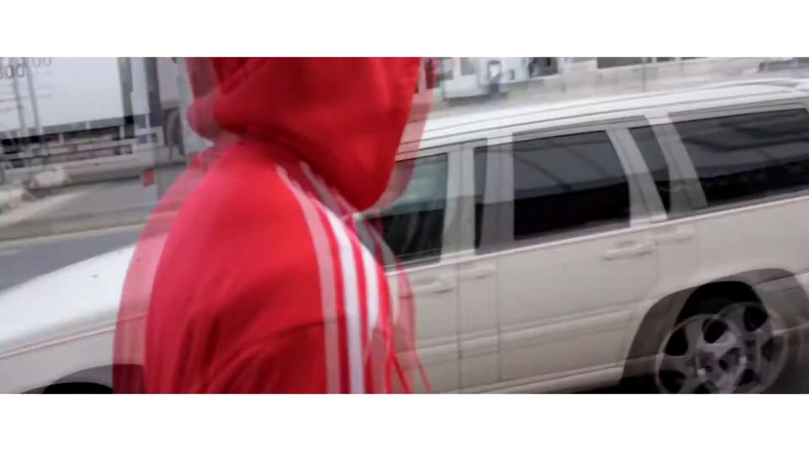 a man in a red hoodie walking past a white car