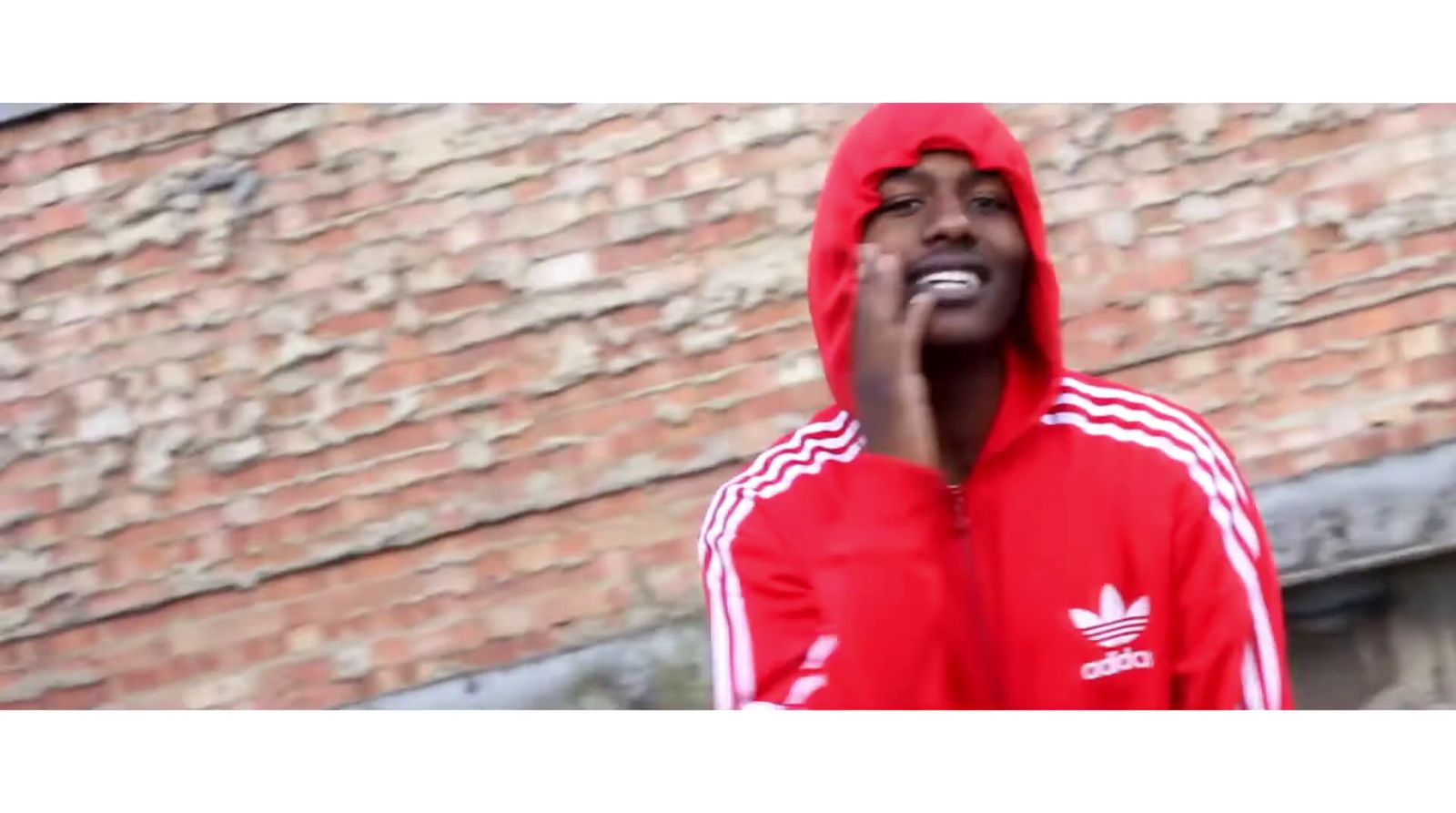 a man in a red adidas hoodie standing in front of a brick wall