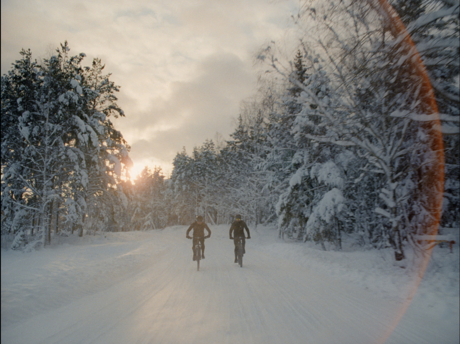 a couple of people riding bikes down a snow covered road