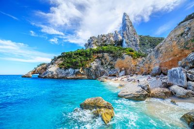 a rocky beach with blue water and people on it