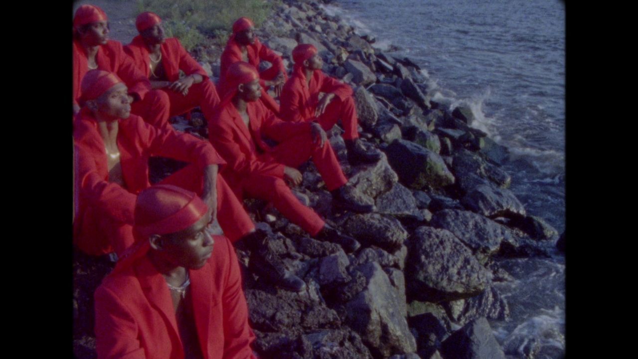 a group of people in red suits sitting on rocks by the water