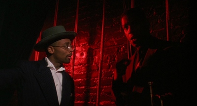 a man in a suit and hat standing in front of a brick wall