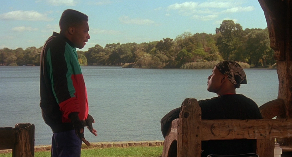 a man standing next to a man sitting on a bench