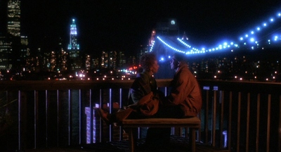 two people sitting on a bench in front of a city at night