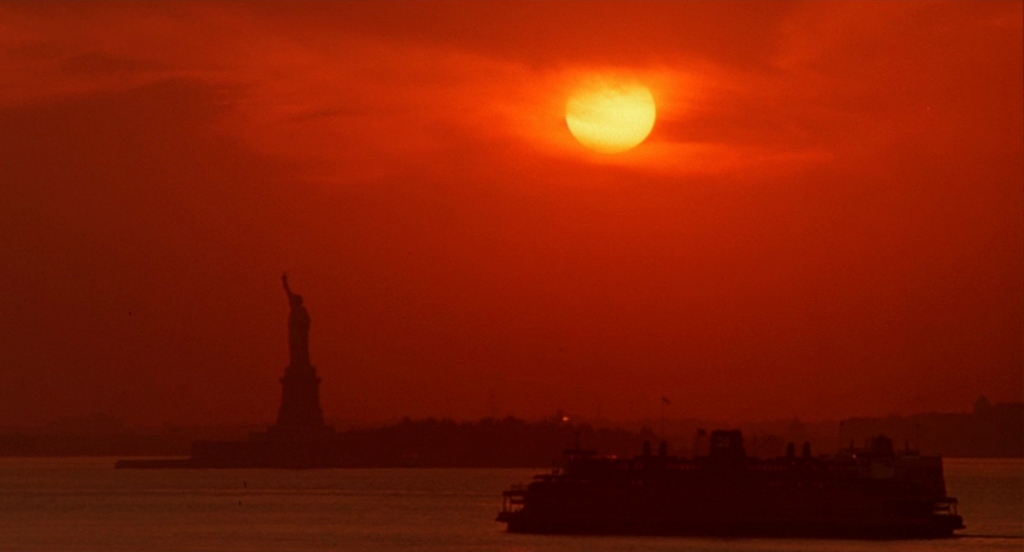 the sun is setting over the statue of liberty