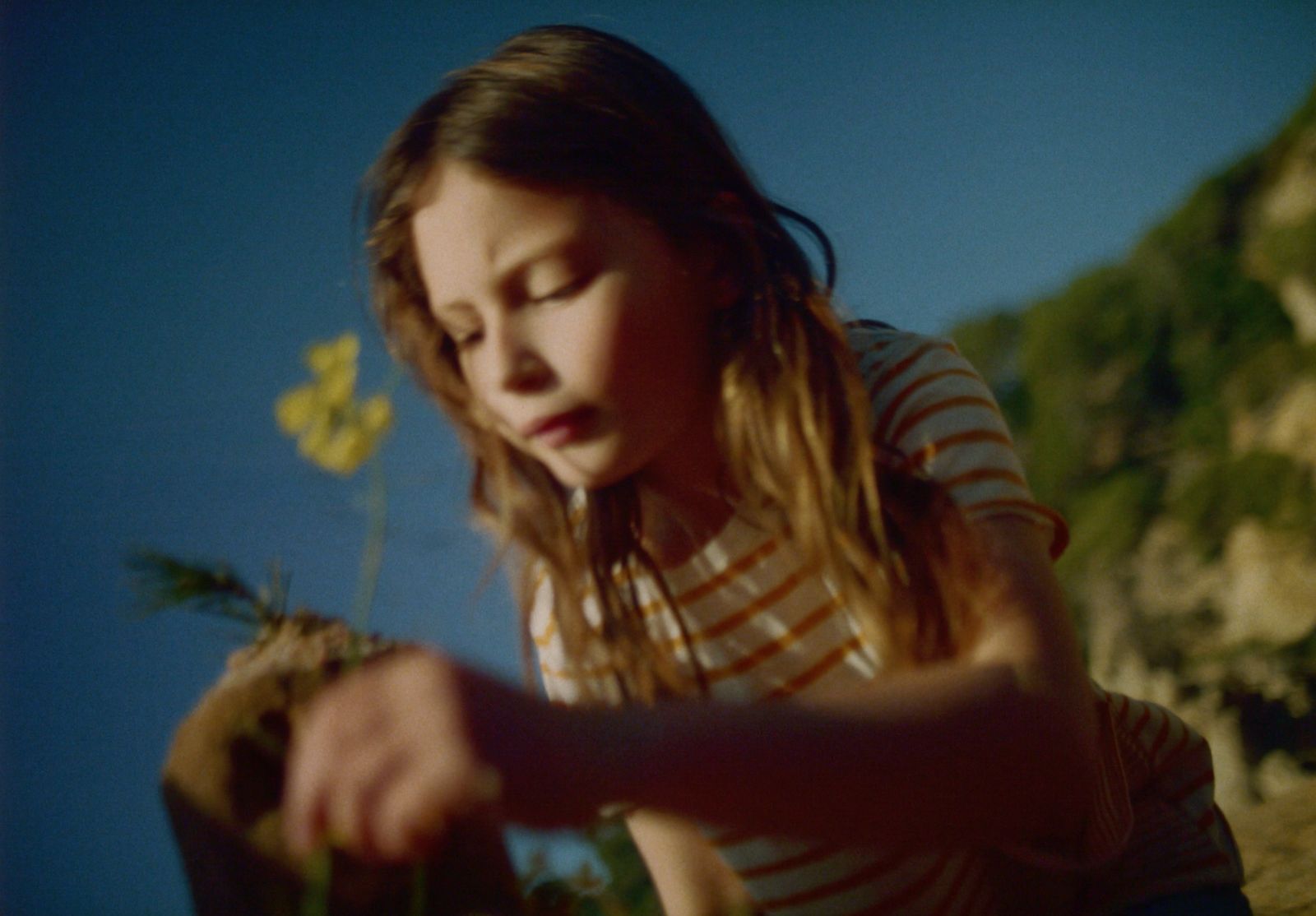 a girl sitting on a rock with a flower in her hand