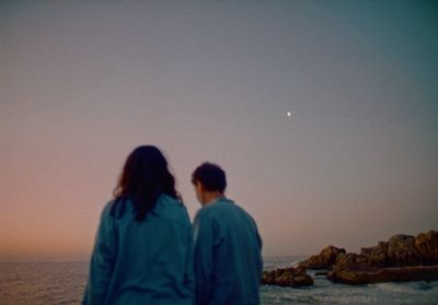 a couple of people standing next to each other near the ocean