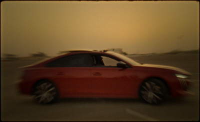 a red car driving down a street with a sky background