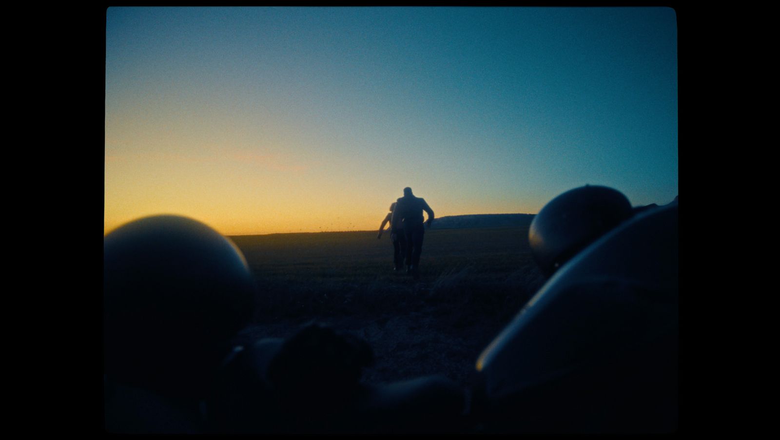 a man walking through a field at sunset