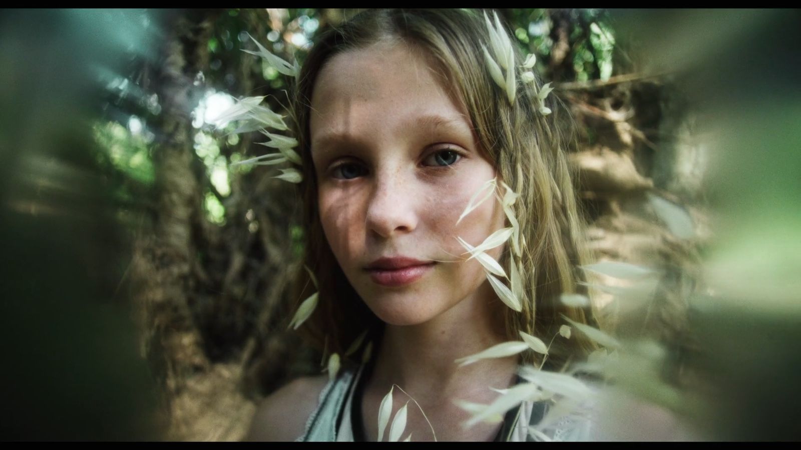 a young girl standing in a forest looking at the camera