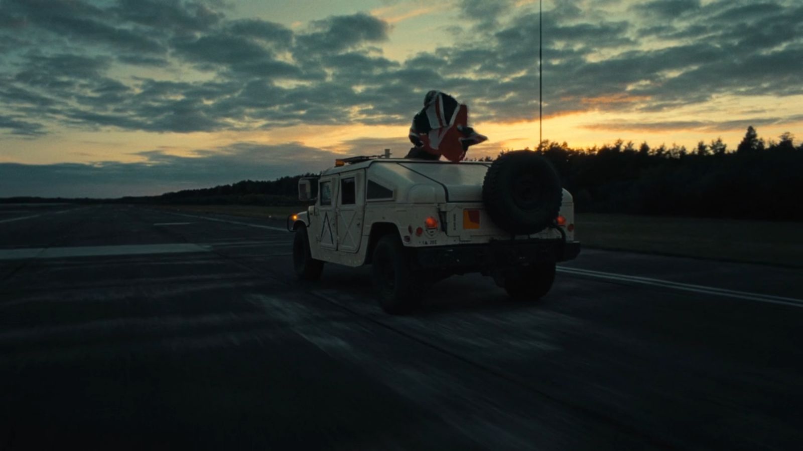 a military vehicle driving down a road at dusk