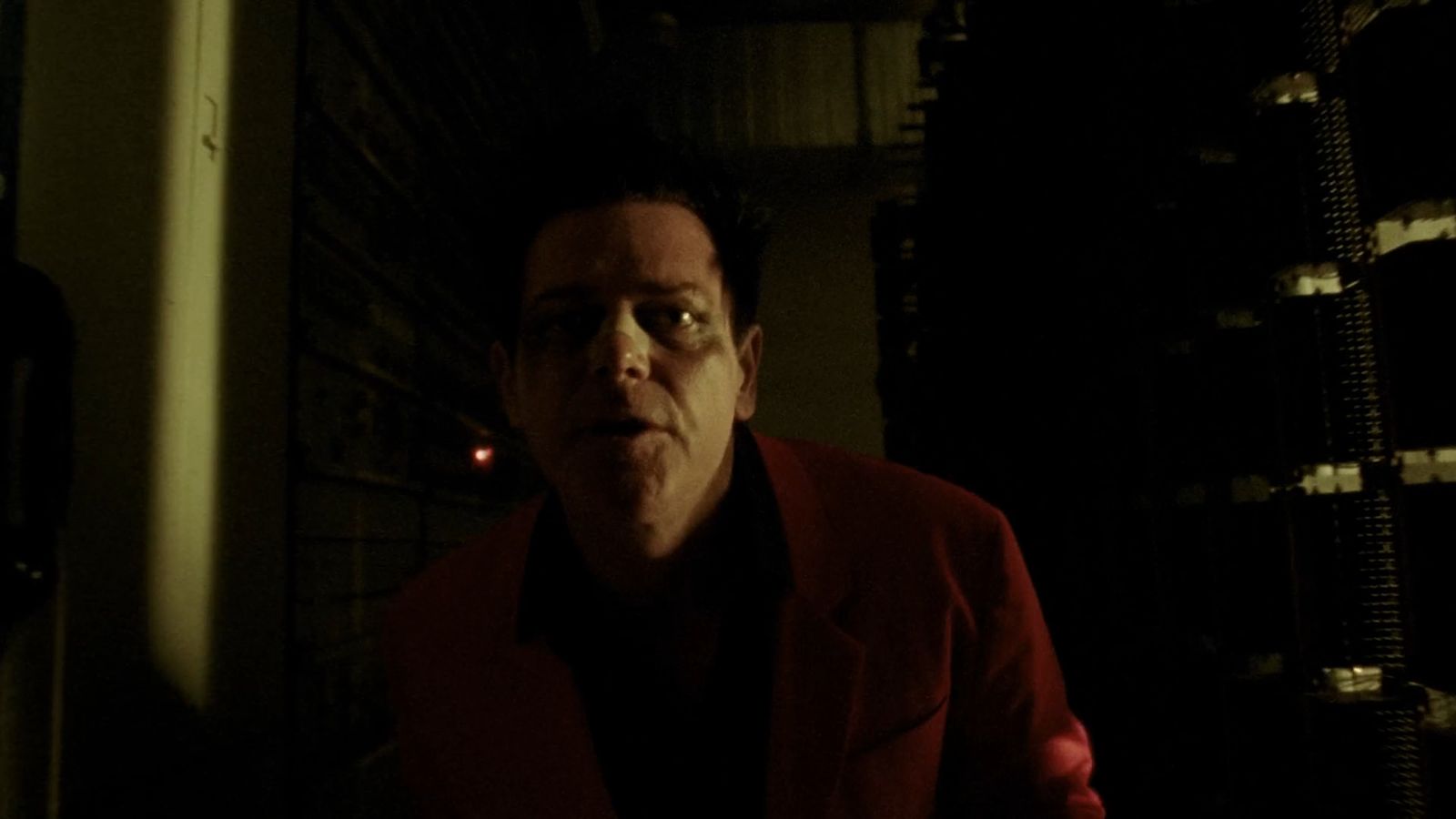 a man in a red jacket standing in a dark room