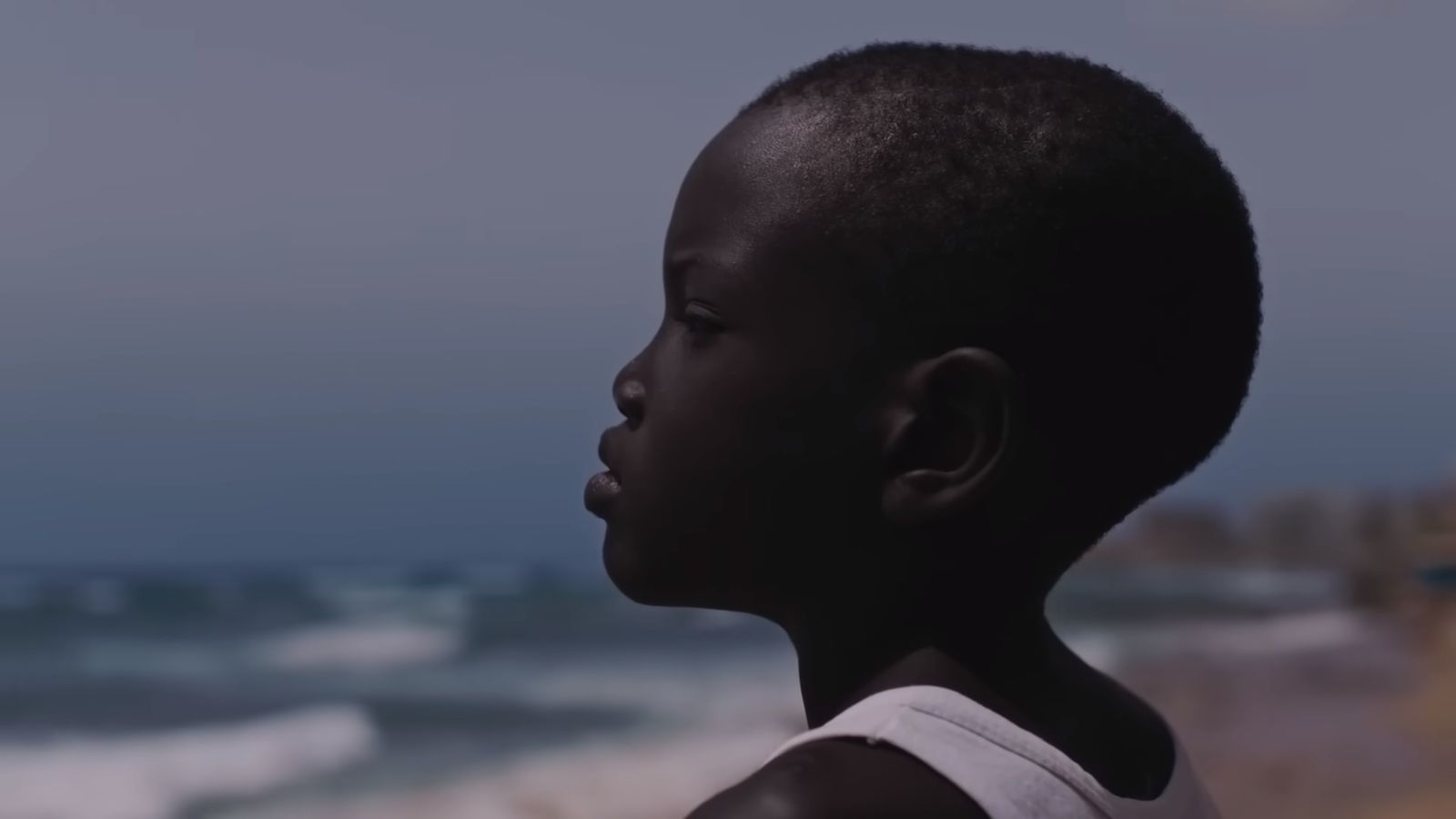 a young boy standing on a beach next to the ocean