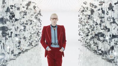 a man in a red suit standing in front of a wall of mirrors