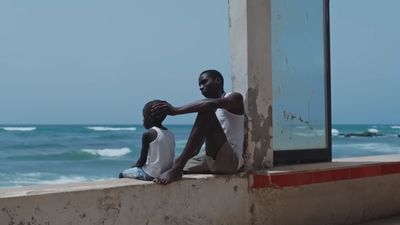 a man and a woman sitting on a ledge near the ocean