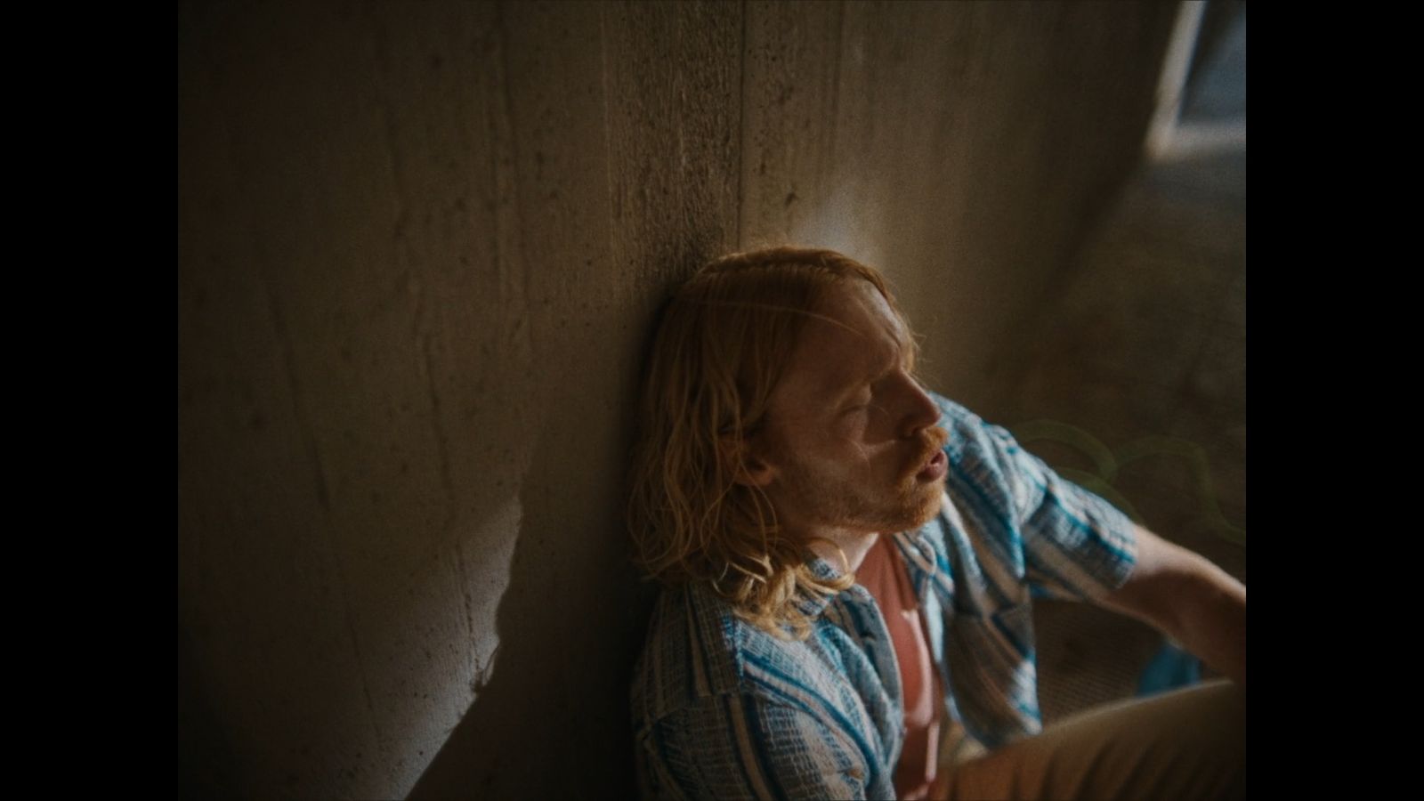 a man with long hair sitting against a wall