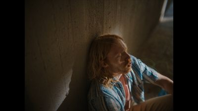 a man with long hair sitting against a wall