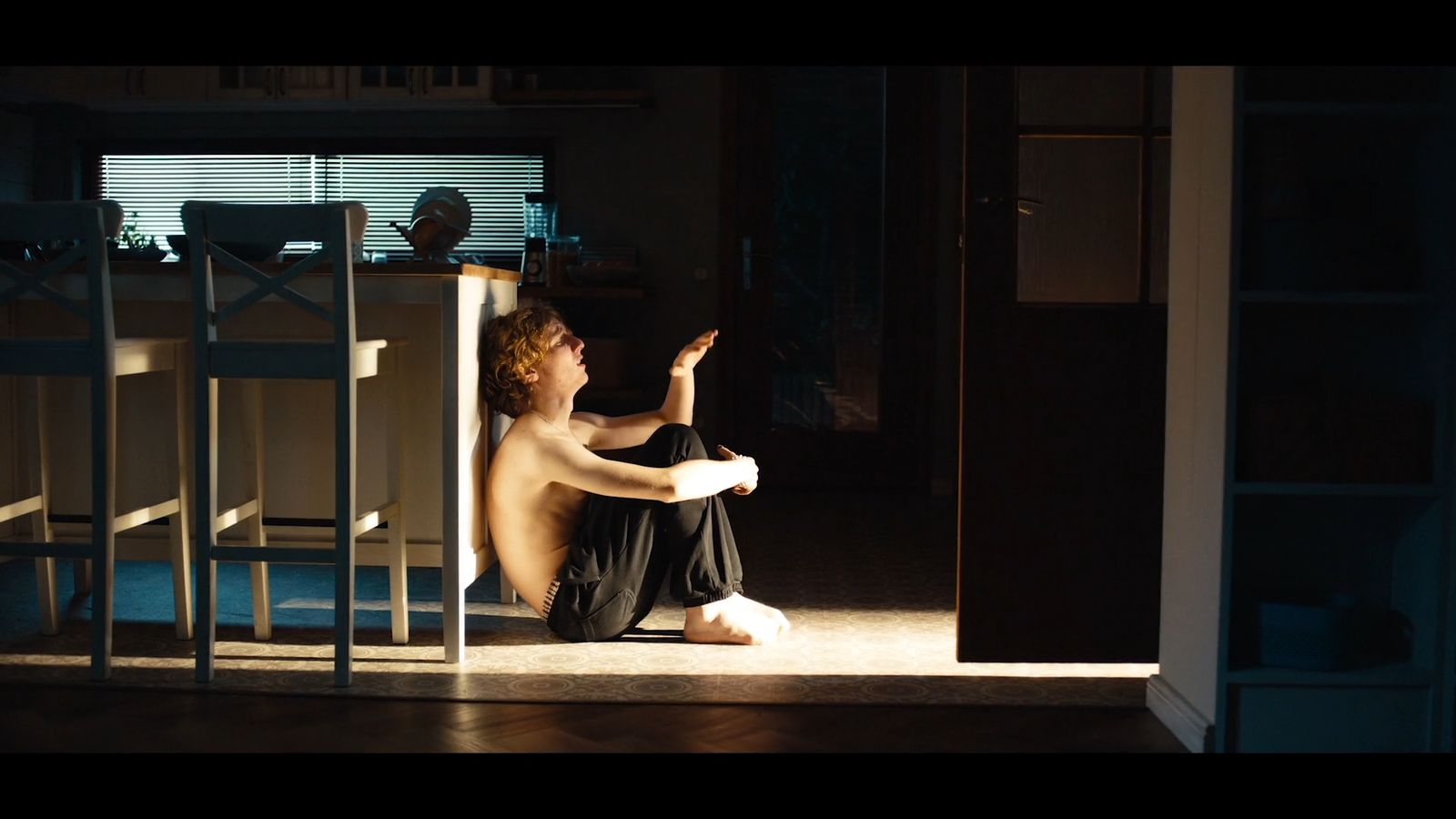 a shirtless man sitting on the floor in a dark room