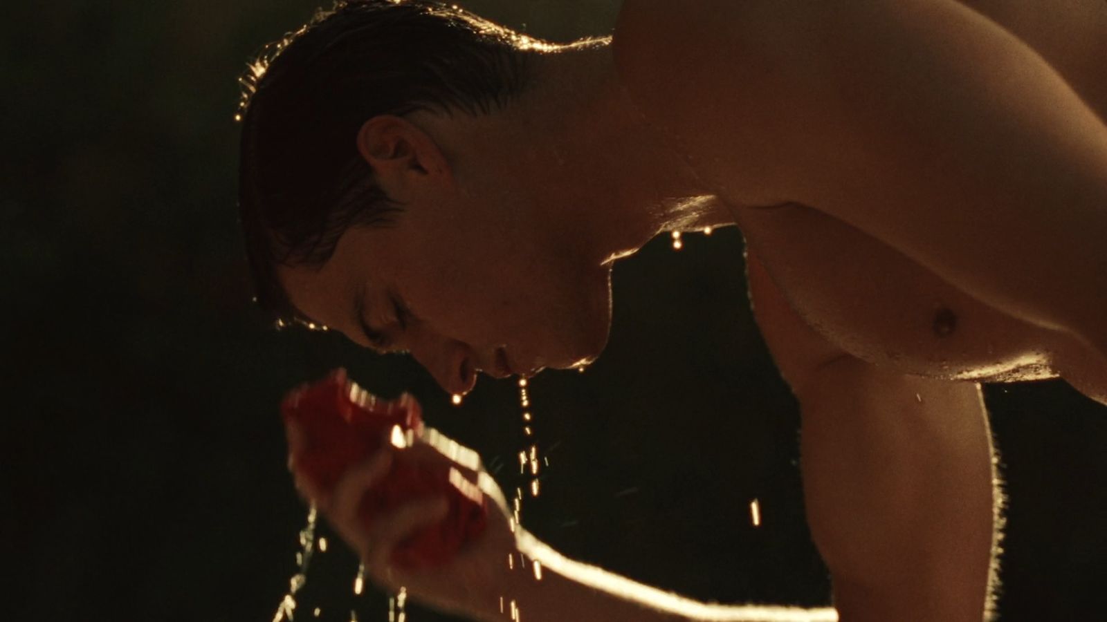 a shirtless man is drinking water from a faucet