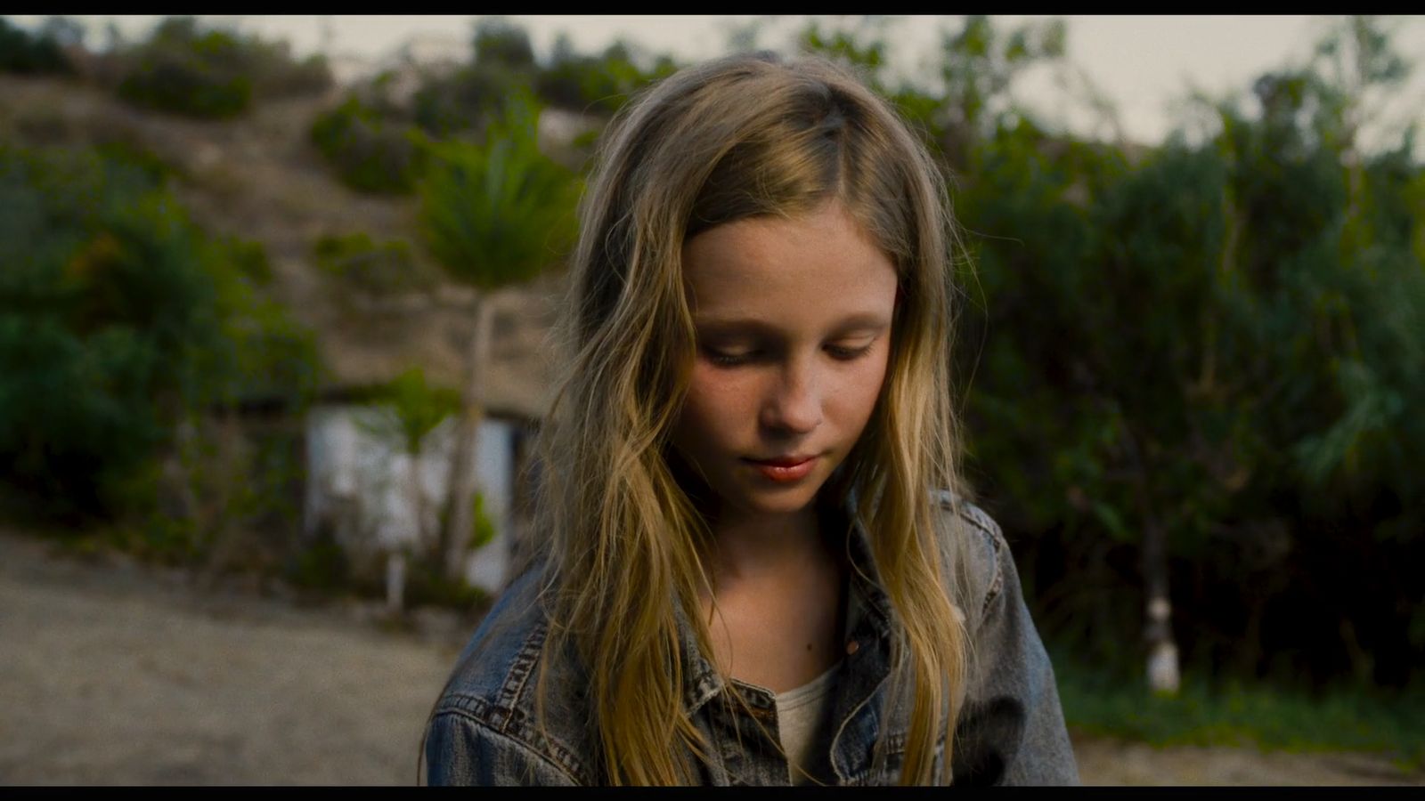 a young girl with long blonde hair looking down at her cell phone